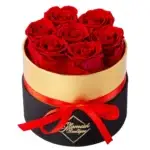 Round black and gold gift box containing seven vibrant preserved red roses