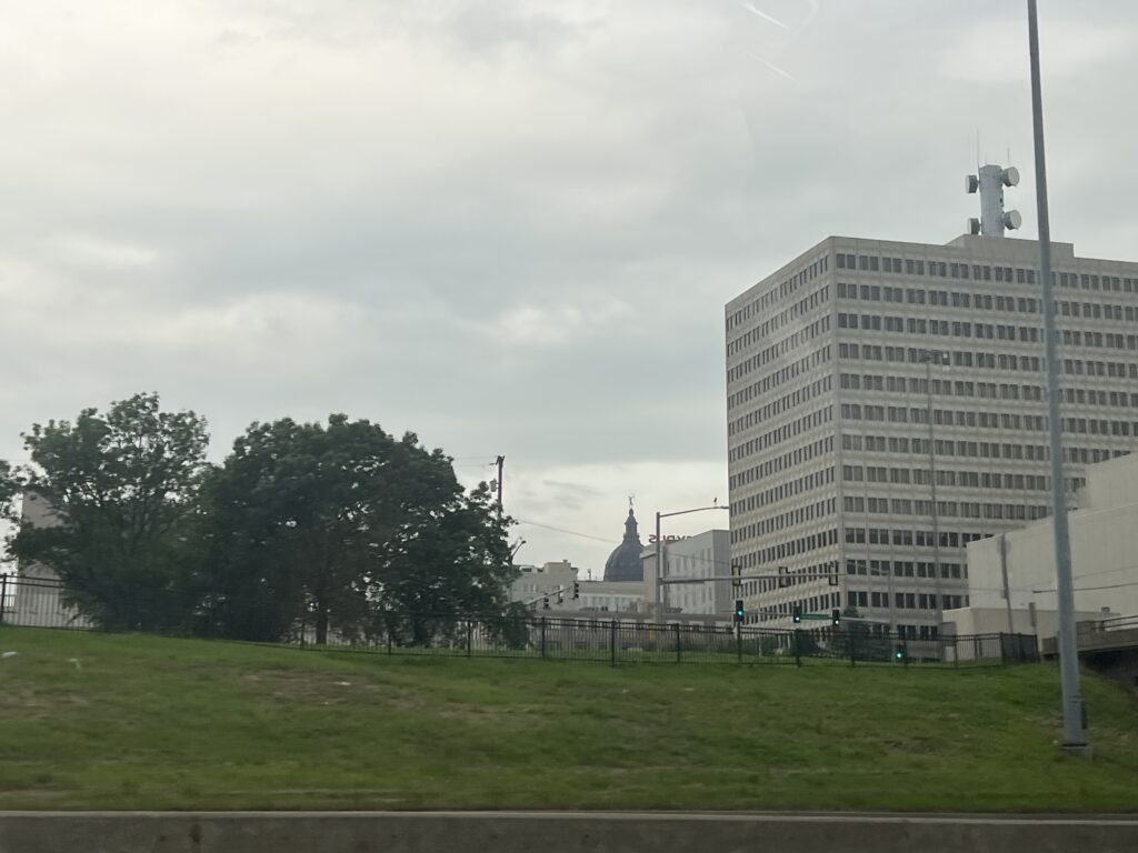 View of the Kansas State Capitol dome peeking between downtown Topeka buildings on a sunny day
