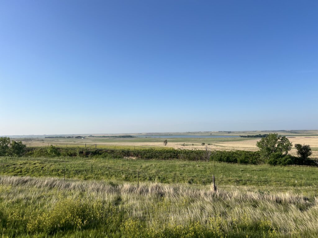 Wide open Kansas landscape with rolling fields and expansive blue sky.