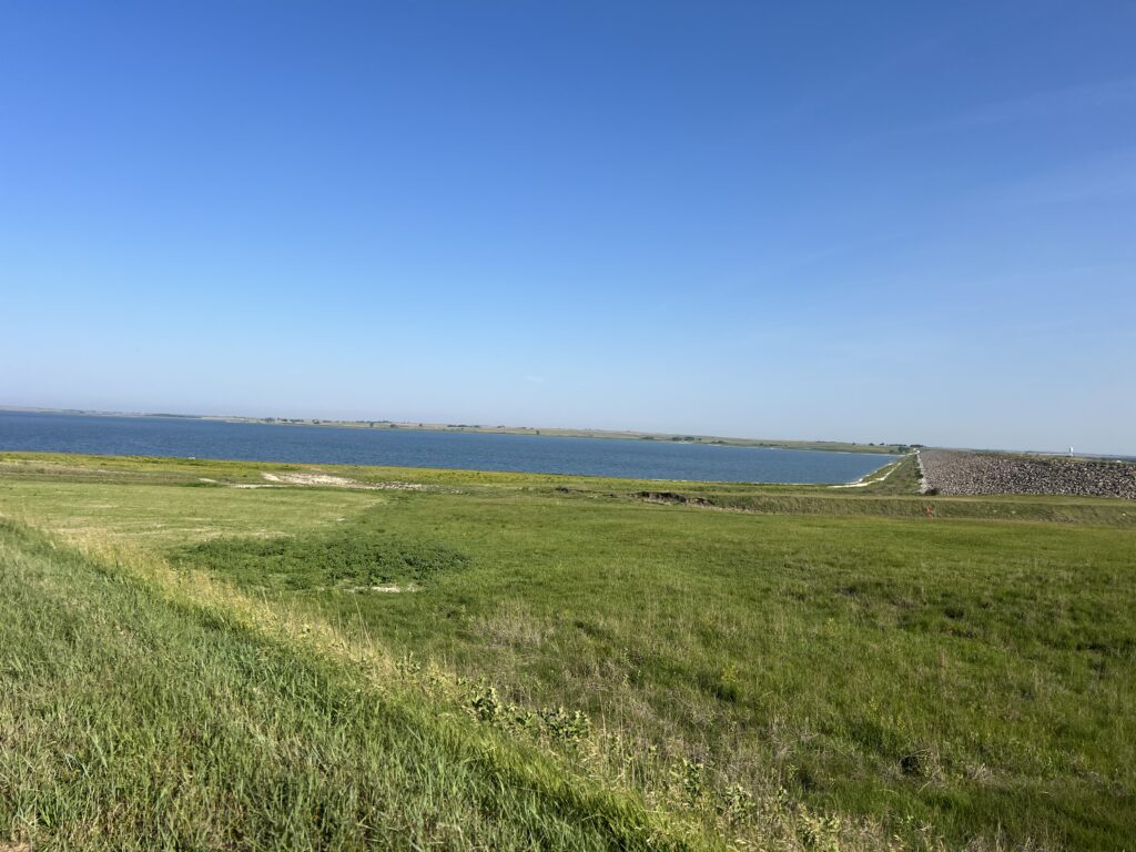 Peaceful Kansas landscape with open fields, scattered trees, and a small lake reflecting the sky.