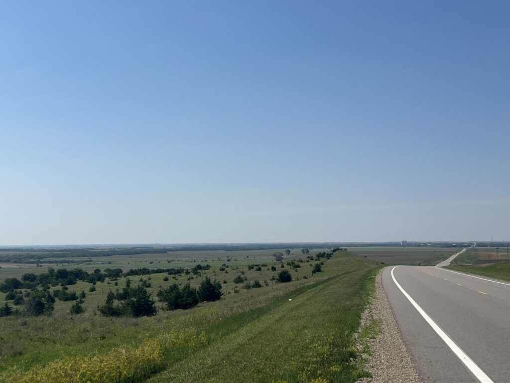 Expansive Kansas landscape with endless skies, dotted with farmland and gently rolling plains bathed in soft sunlight.