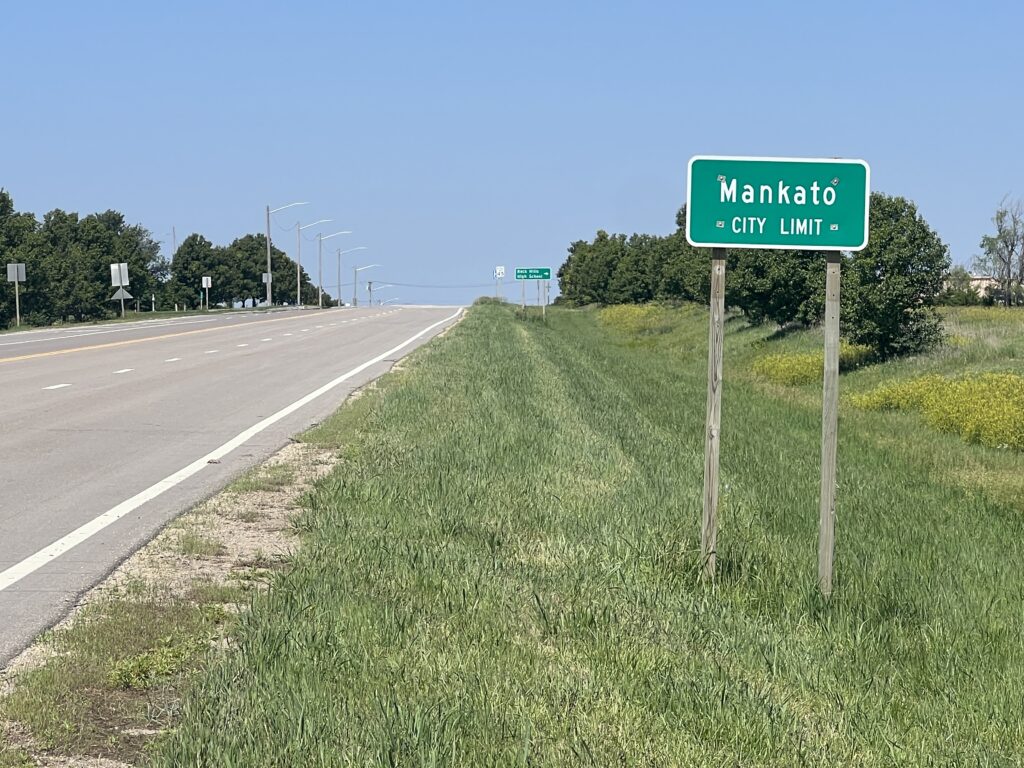 Welcome sign for the town of Mankato, Kansas, set against a backdrop of open sky and rural landscape.