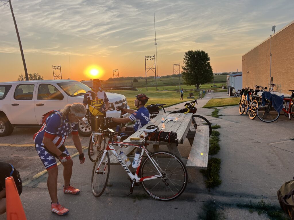 Bicycles lined up and ready to roll with the morning sun rising behind them, casting a warm glow over the start of Day 5 of Biking Across Kansas.