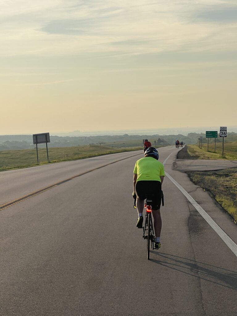 Solo bike parked on the shoulder of a long, empty highway winding through rolling Kansas hills.