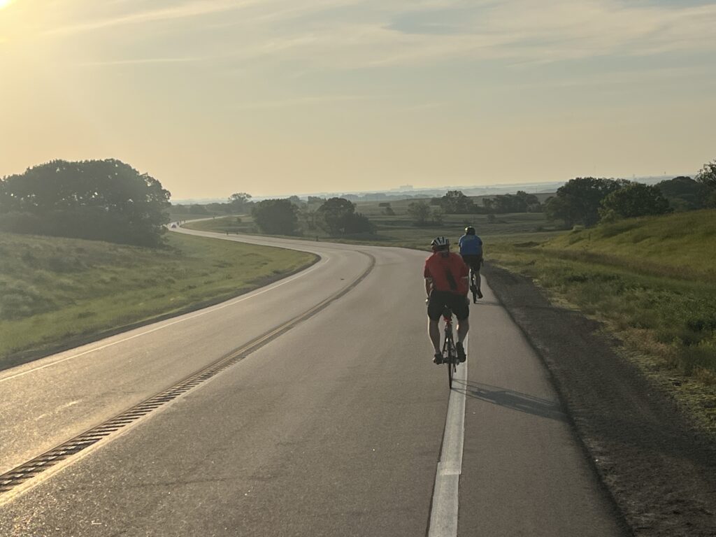 A bicycle resting on the side of a quiet highway stretching through Kansas farmland under a bright sky.