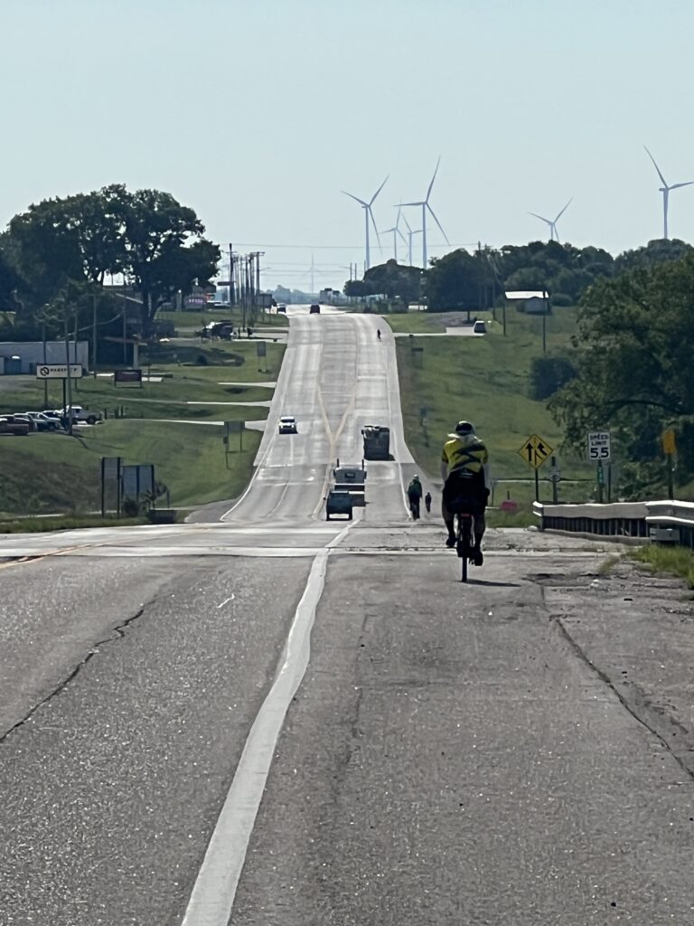 A towering windmill beside a traditional farmhouse set against the expansive Kansas prairie landscape.
