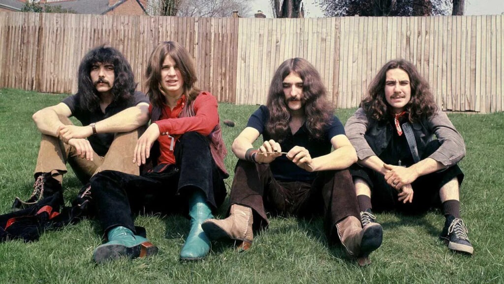 Early Black Sabbath band members sitting on a lawn, looking young and relaxed