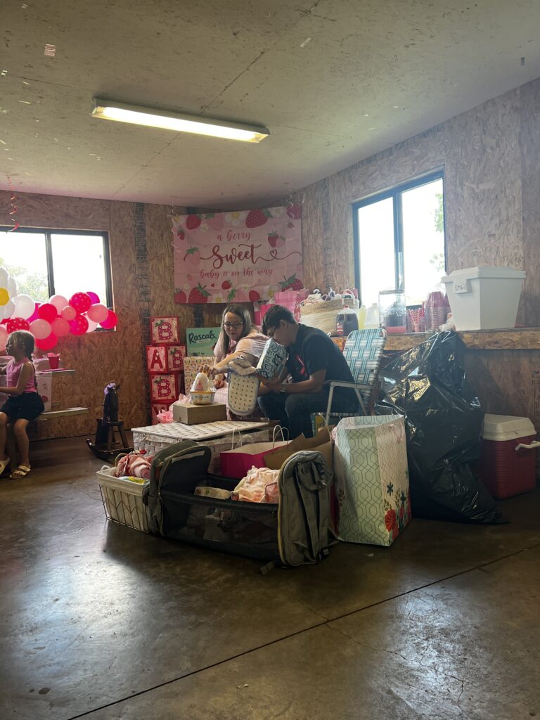 Marla and Brylan smiling and looking up from reading cards during the baby shower, pausing to thank the people around them.