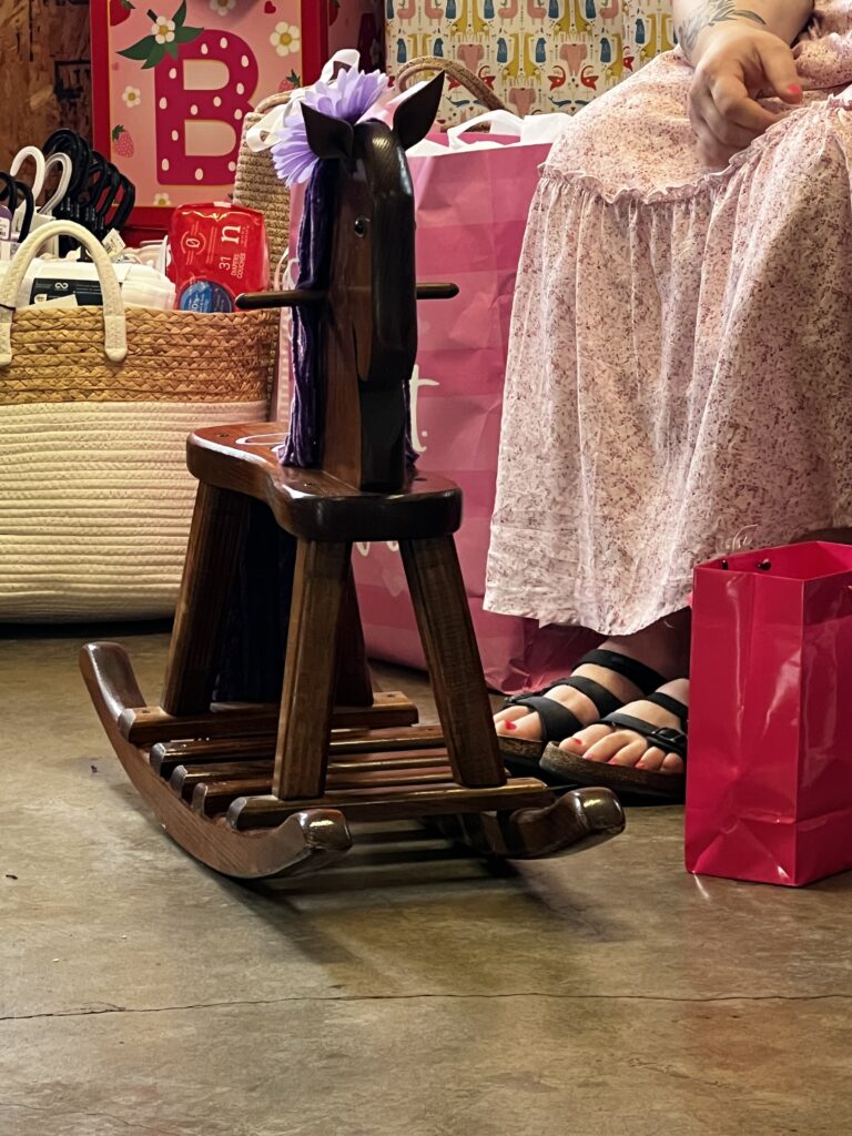 Wooden rocking horse surrounded by wrapped baby shower gifts.