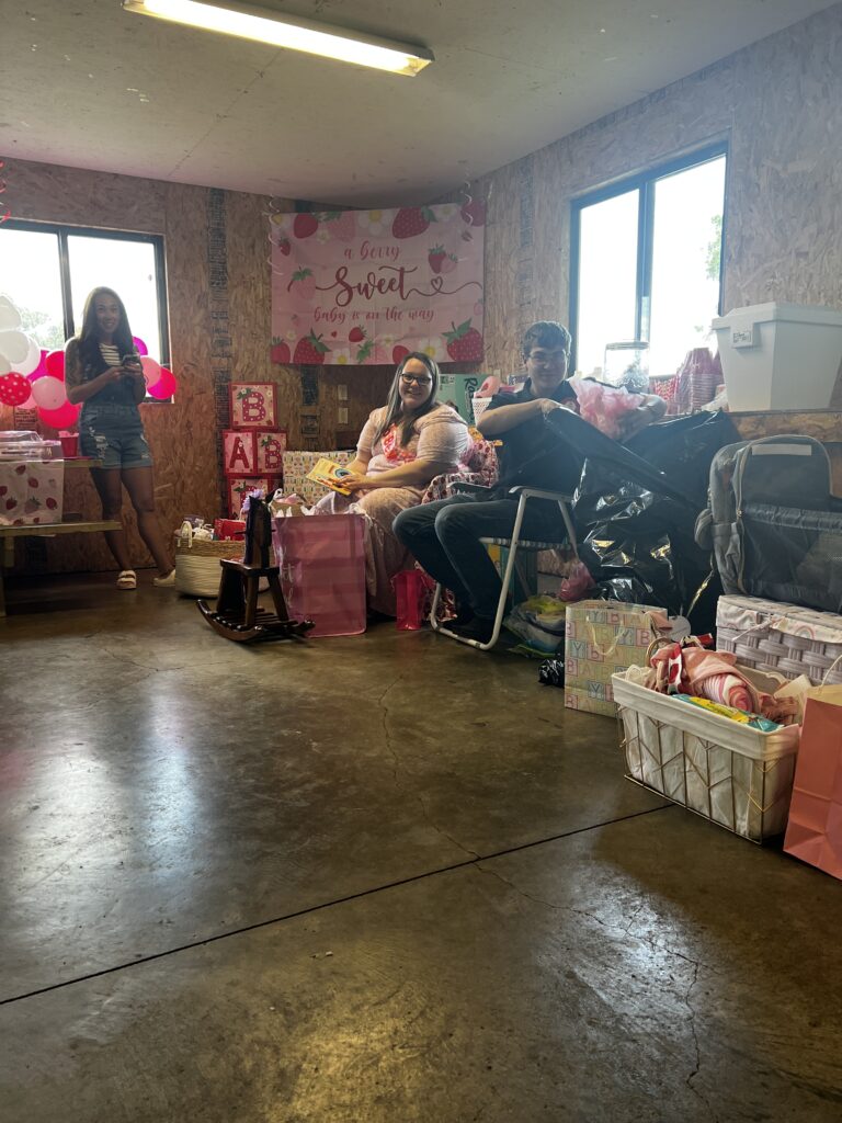 Brylan throwing wrapping paper into a trash bag as Marla looks on during the baby shower gift opening.