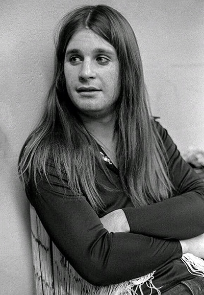 Ozzy Osbourne in his early years, sitting with long hair and arms folded