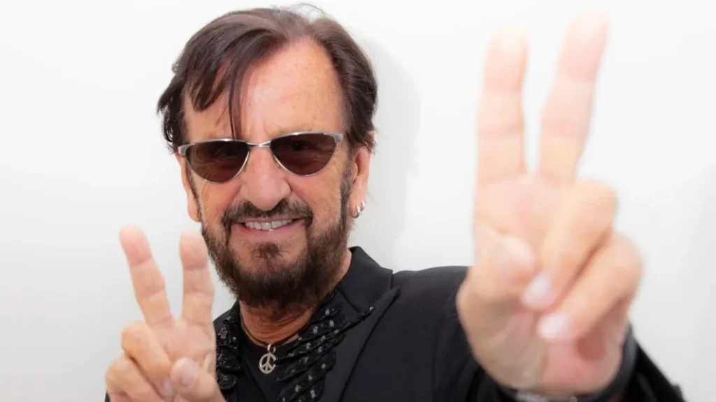 Ringo Starr in his 80s, smiling and flashing a peace sign, embodying decades of music, peace, and resilience.