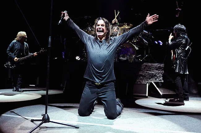 Ozzy Osbourne on his knees with arms spread wide like an eagle during a live performance