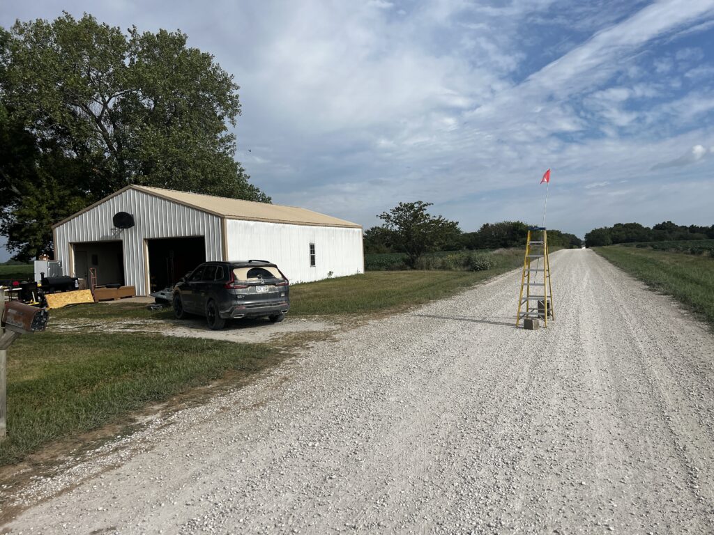 Dirt road with a makeshift 14-foot ladder barrier and flag to slow traffic.