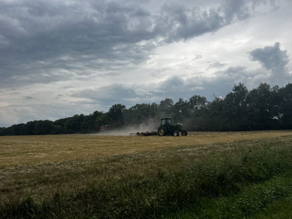 John Deere tractor working in a field along the scenic route to Princeton, Kansas, with clouds overhead and farmland stretching into the distance.