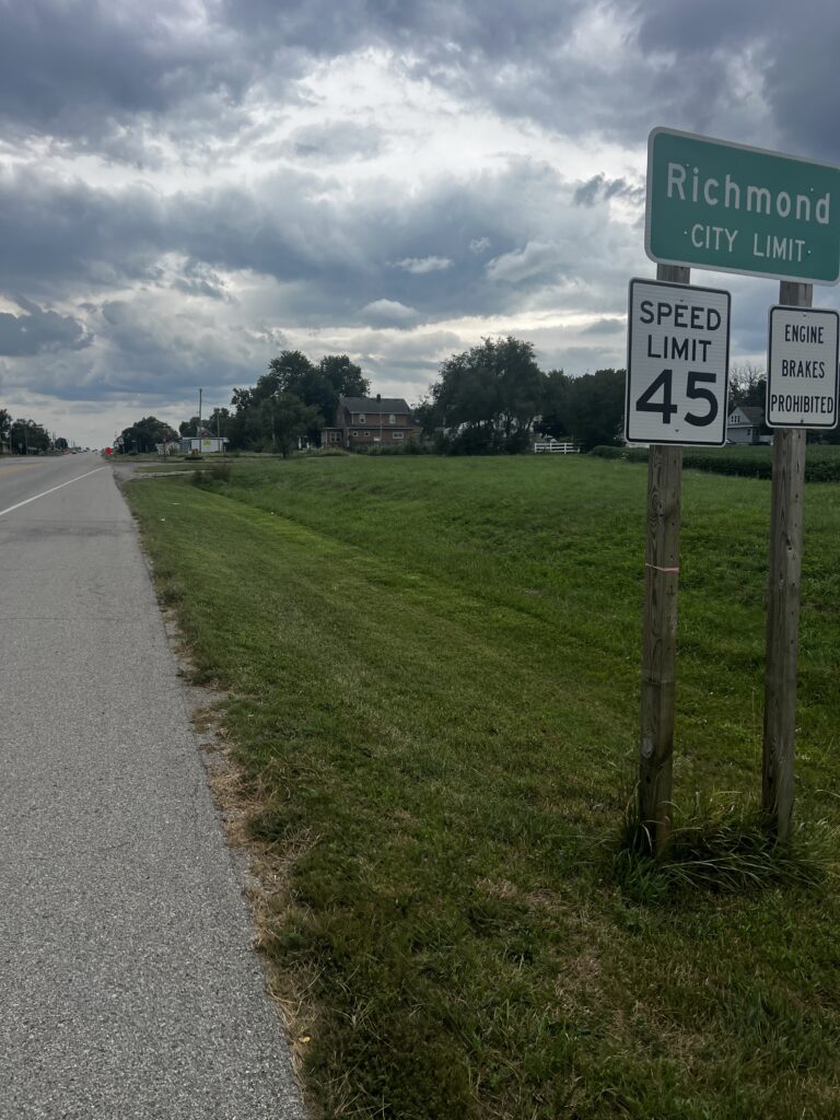 Cyclist approaching the town sign of Richmond, Kansas, with a welcoming view of the town's main street and countryside.