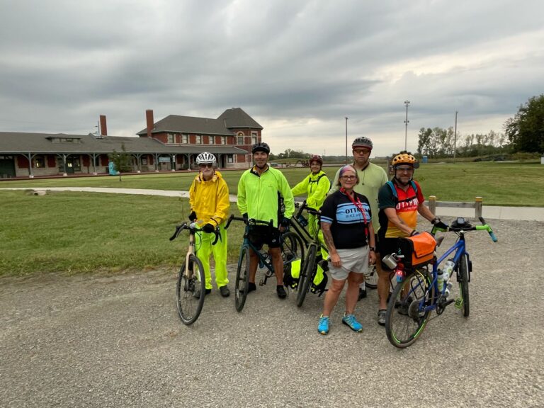 Group of cyclists at Sedalia Depot on the Katy Trail 2025, posing for a photo with bikes and gear in the background.