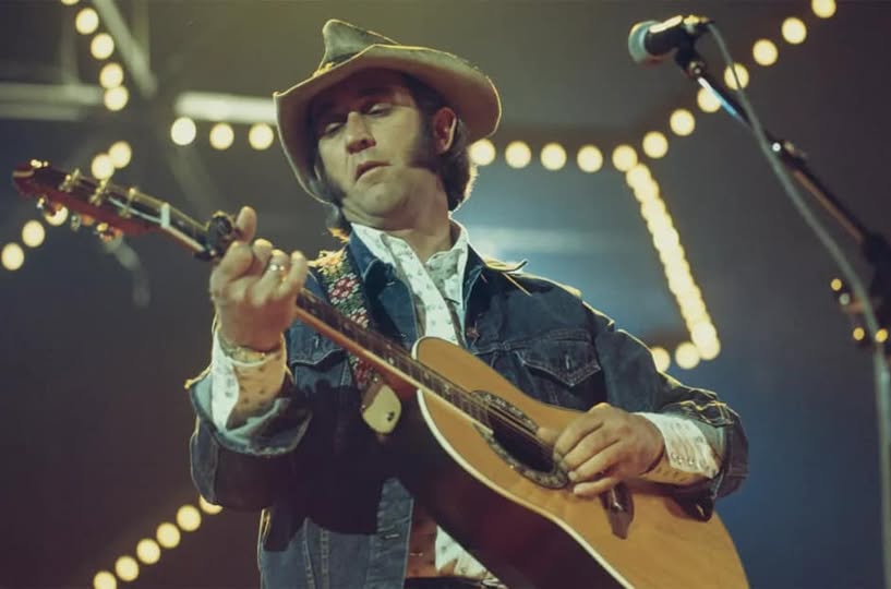 Don Williams performing on stage, singing into a microphone, wearing a classic country outfit, spotlight highlighting his face.