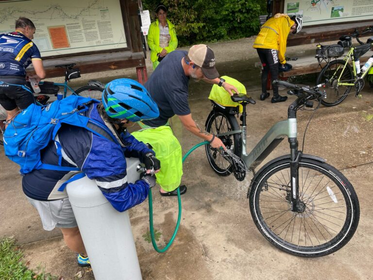 Cyclists rinsing all bikes with a hose at Boonville Trailhead on the Katy Trail after a rainy ride.