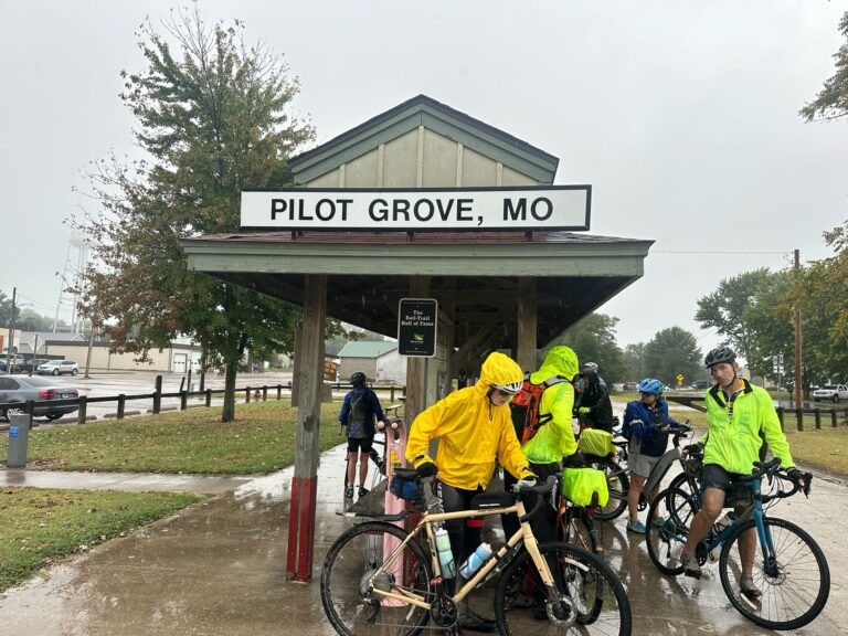 Cyclists at Pilot Grove Trailhead rinsing off bikes and bags after riding the Katy Trail in rain and crushed limestone.