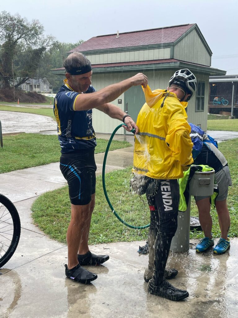 Robert using a hose to rinse off other cyclists at Boonville Trailhead on the Katy Trail after a rainy ride.