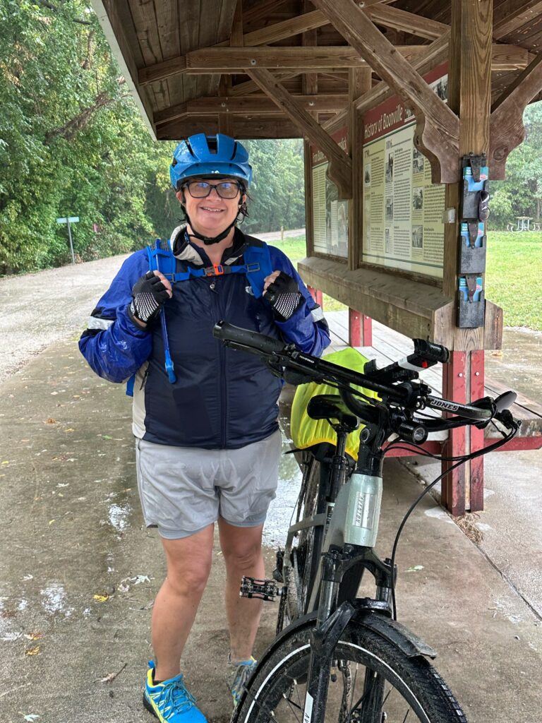 Tammy standing tall at Boonville Trailhead on the Katy Trail, soaked from rain but smiling.