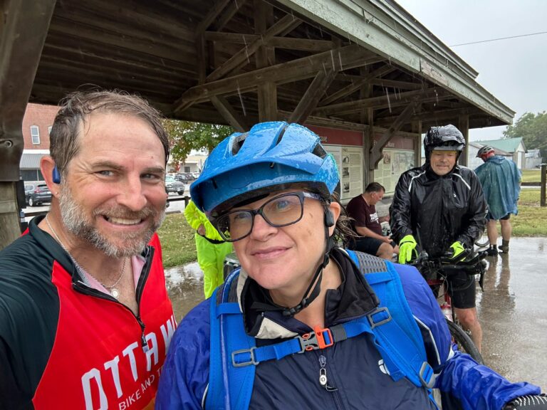 Larbe and his wife Tammy standing soaked in rain gear on the Katy Trail after riding through heavy rain.