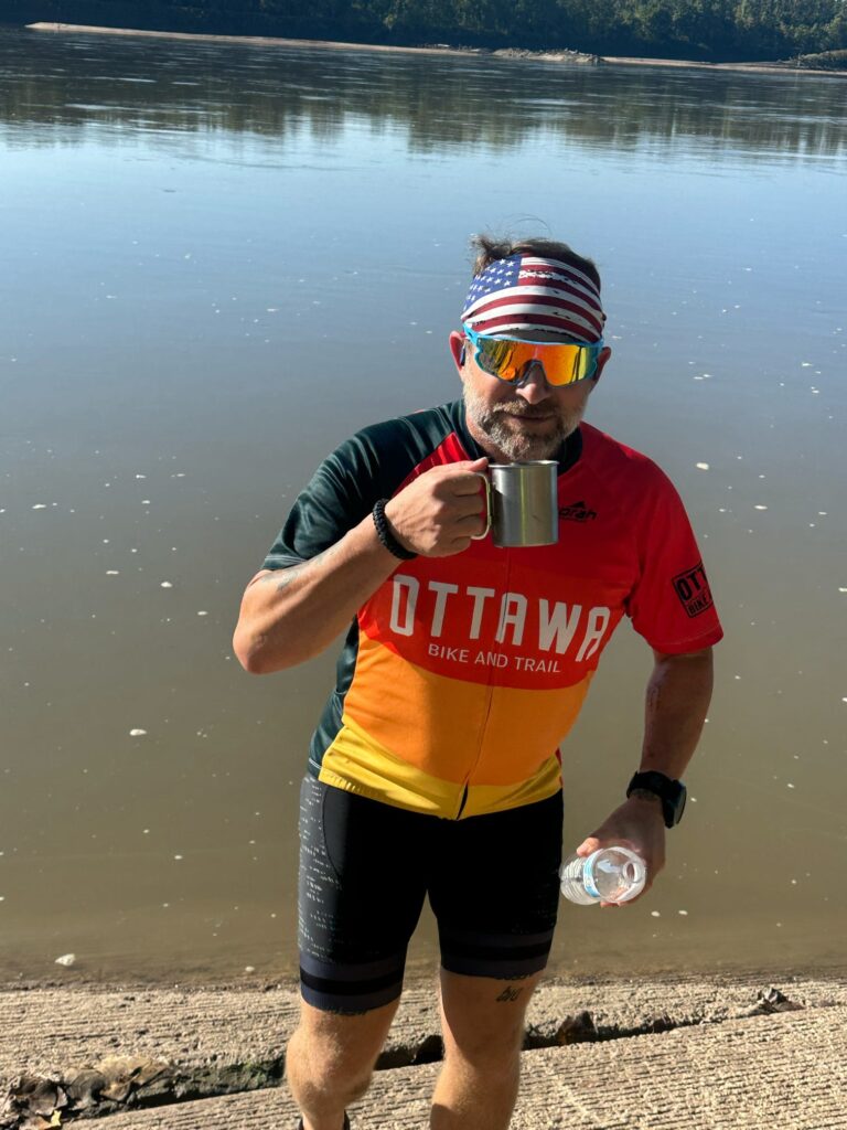 Larabe standing at the banks of the Missouri River with a miner’s cup in hand, ready to dip from the river.