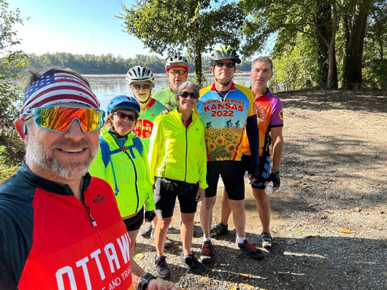 Our group standing together with hats on, smiling in front of the Missouri River.