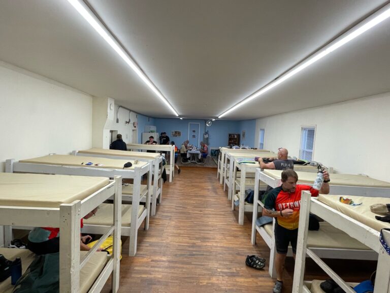 Inside the Turner Katy Trail Shelter in Tebbetts, Missouri with bunk beds, kitchen area, and riders preparing their beds