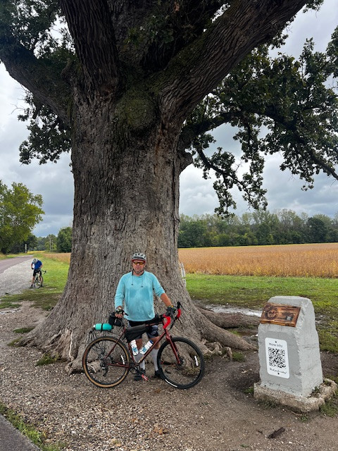 Shaune standing with his bike next to a large lone pin oak tree in a field