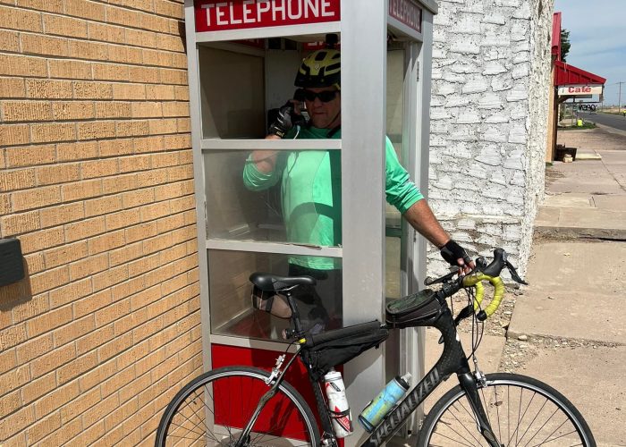Shaune standing in a phone booth with his bicycle in Coolidge, Kansas, shared by ShauneNation.