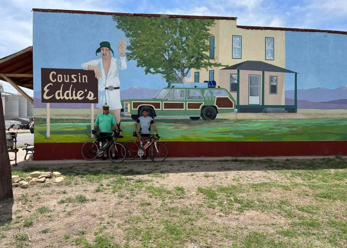 Shaune and Rob standing in front of the Cousin Eddie mural in Coolidge, Kansas, featuring scenes from National Lampoon's Vacation